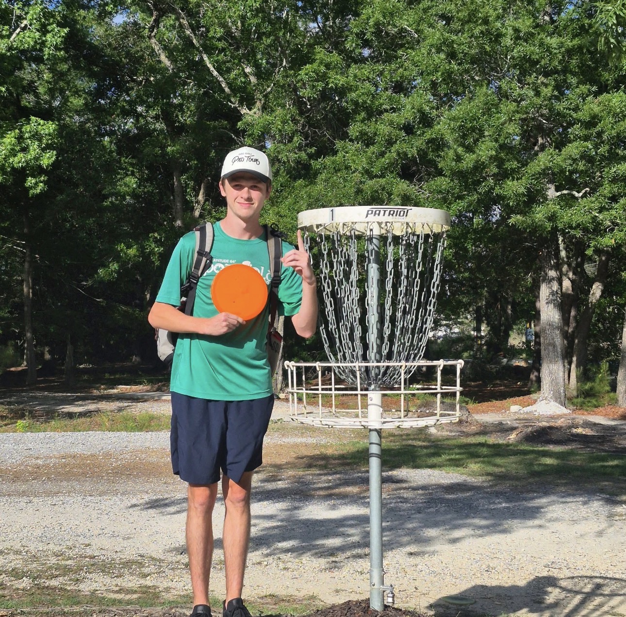 Luke McElroy smiling on the disc golf course with an orange disc